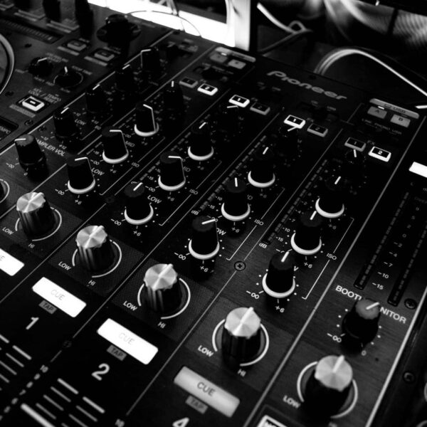Black and white close-up of a DJ's audio mixing console with knobs and controls. Omen