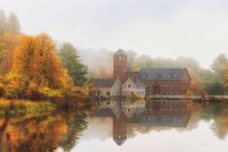 Road trip, Northeast, Serene autumn scene with a historic mansion and vibrant foliage reflected on still water.