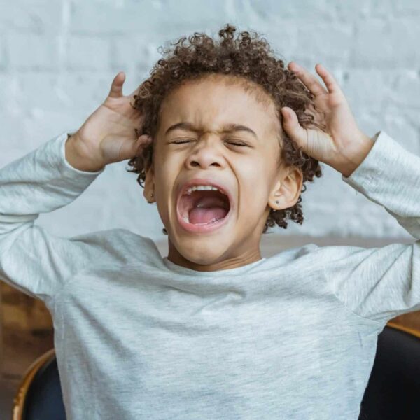 Young boy showing frustration indoors with hands on head, eyes closed, mouth open, spoiled child. parenting