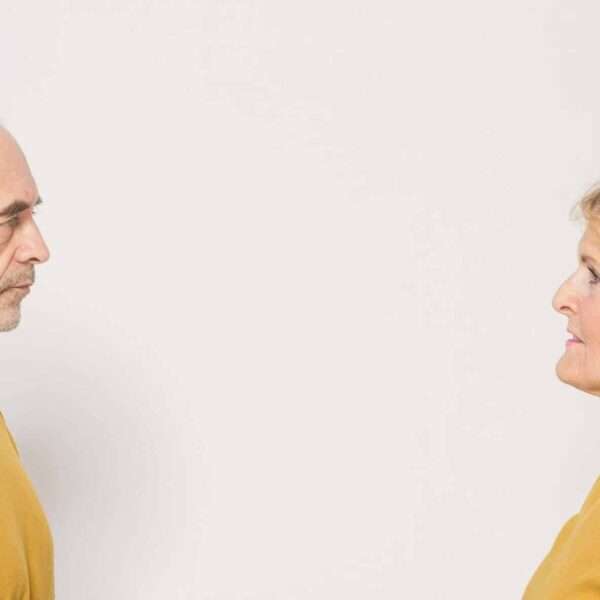 An elderly couple dressed in yellow sweaters facing each other in a studio setting. menodivorce