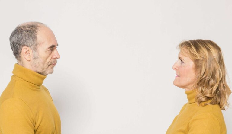 An elderly couple dressed in yellow sweaters facing each other in a studio setting. menodivorce