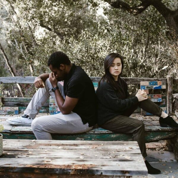 Infidelity, cheating, A couple sits back to back on a wooden bench, indicating a disagreement or breakup.