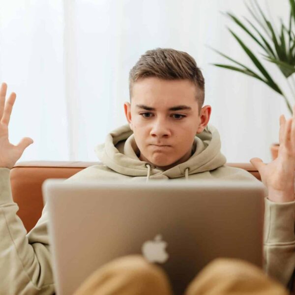 Online radicalization, Teen sitting on couch with laptop, appearing frustrated, indoors.