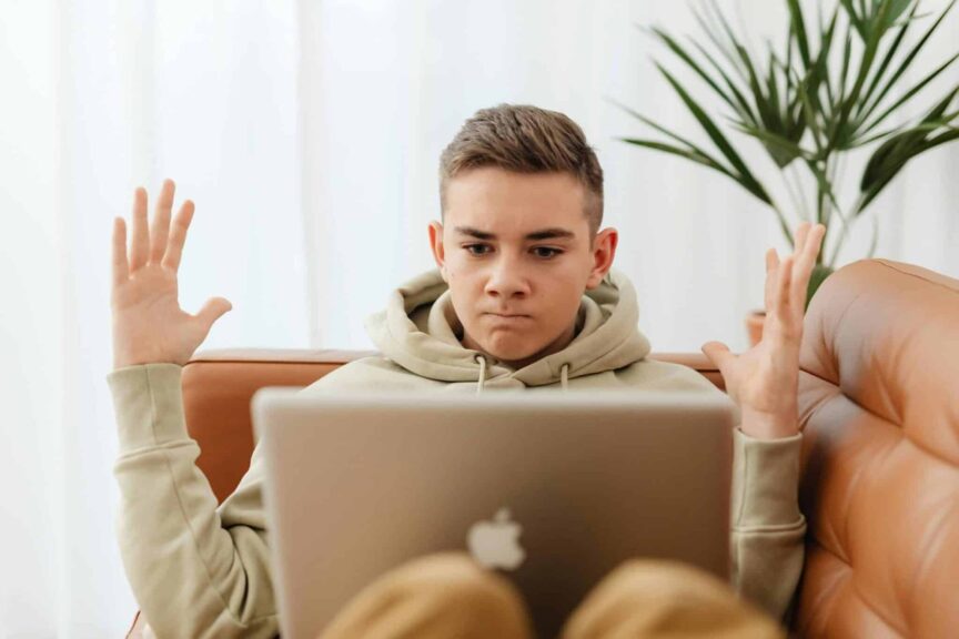 Online radicalization, Teen sitting on couch with laptop, appearing frustrated, indoors.
