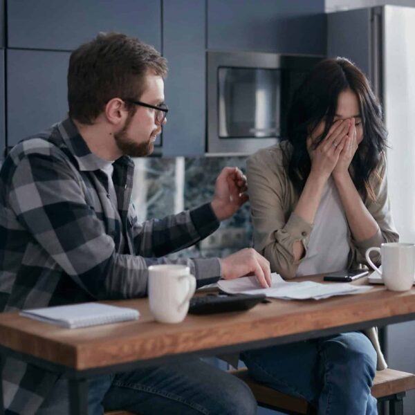 A couple discusses financial issues with bills and a laptop on the table, inside a modern kitchen setting. money