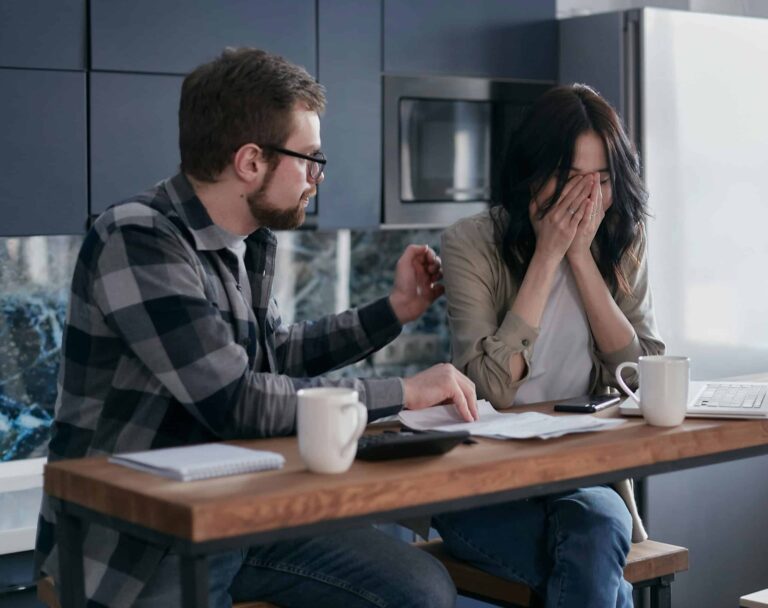 A couple discusses financial issues with bills and a laptop on the table, inside a modern kitchen setting. money