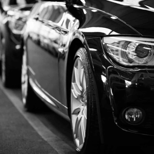 Renting a car, Close-up black and white image of a luxury car line-up focusing on vehicle headlights.