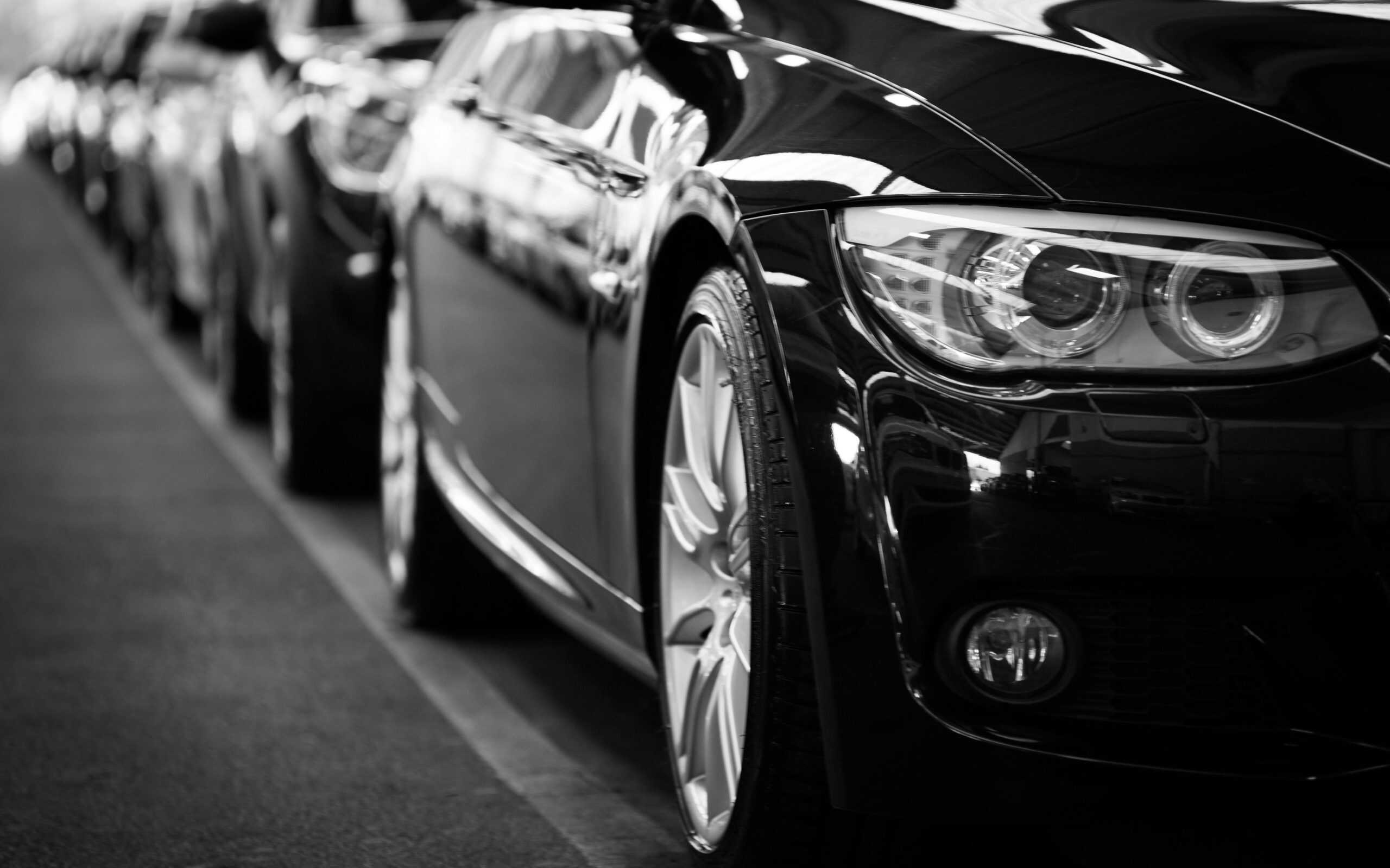Renting a car, Close-up black and white image of a luxury car line-up focusing on vehicle headlights.