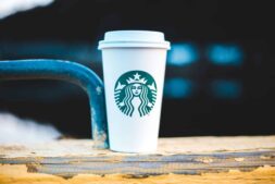 Starbucks A white coffee cup with a logo on a rustic wooden rail, perfect for a cozy outdoor coffee moment.