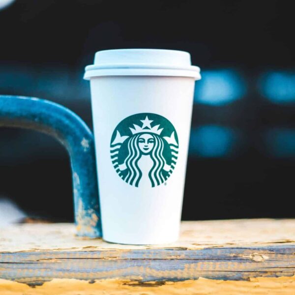 Starbucks A white coffee cup with a logo on a rustic wooden rail, perfect for a cozy outdoor coffee moment.