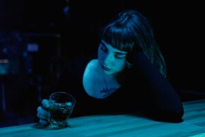 A woman with eyes closed holds a drink at a dim bar. Moody nightlife scene. nonalcoholic drinks