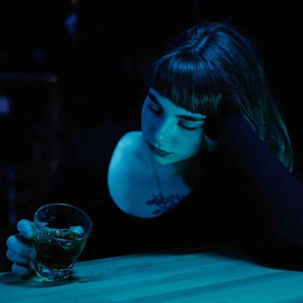 A woman with eyes closed holds a drink at a dim bar. Moody nightlife scene. nonalcoholic drinks