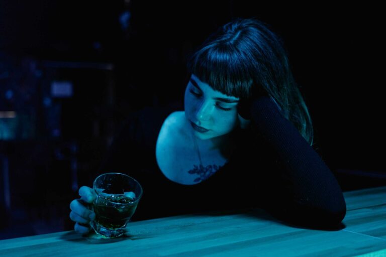 A woman with eyes closed holds a drink at a dim bar. Moody nightlife scene. nonalcoholic drinks