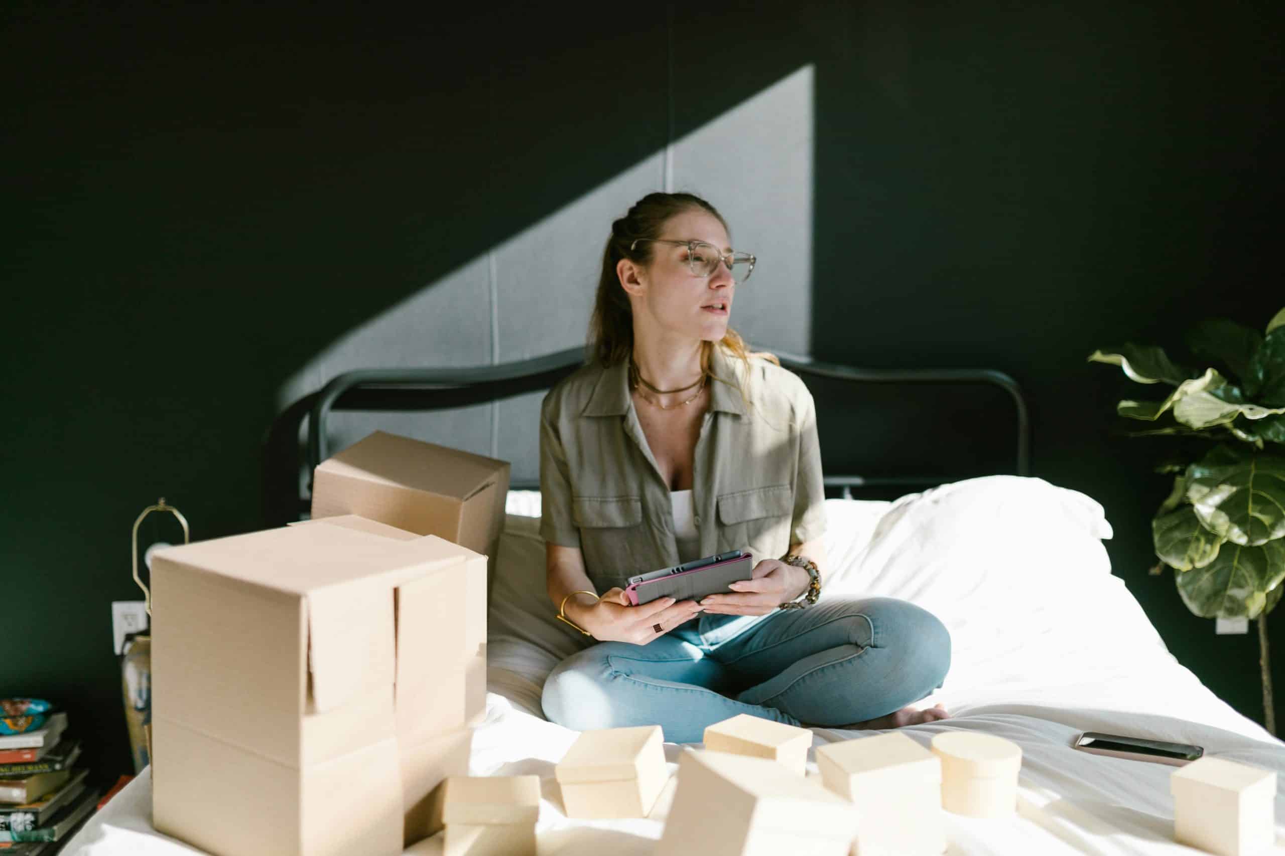 Side hustle, Woman working on e-commerce startup with tablet and boxes on bed.