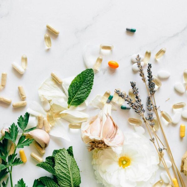 A flatlay of natural herbs, supplements, and flowers on a marble background. creatine