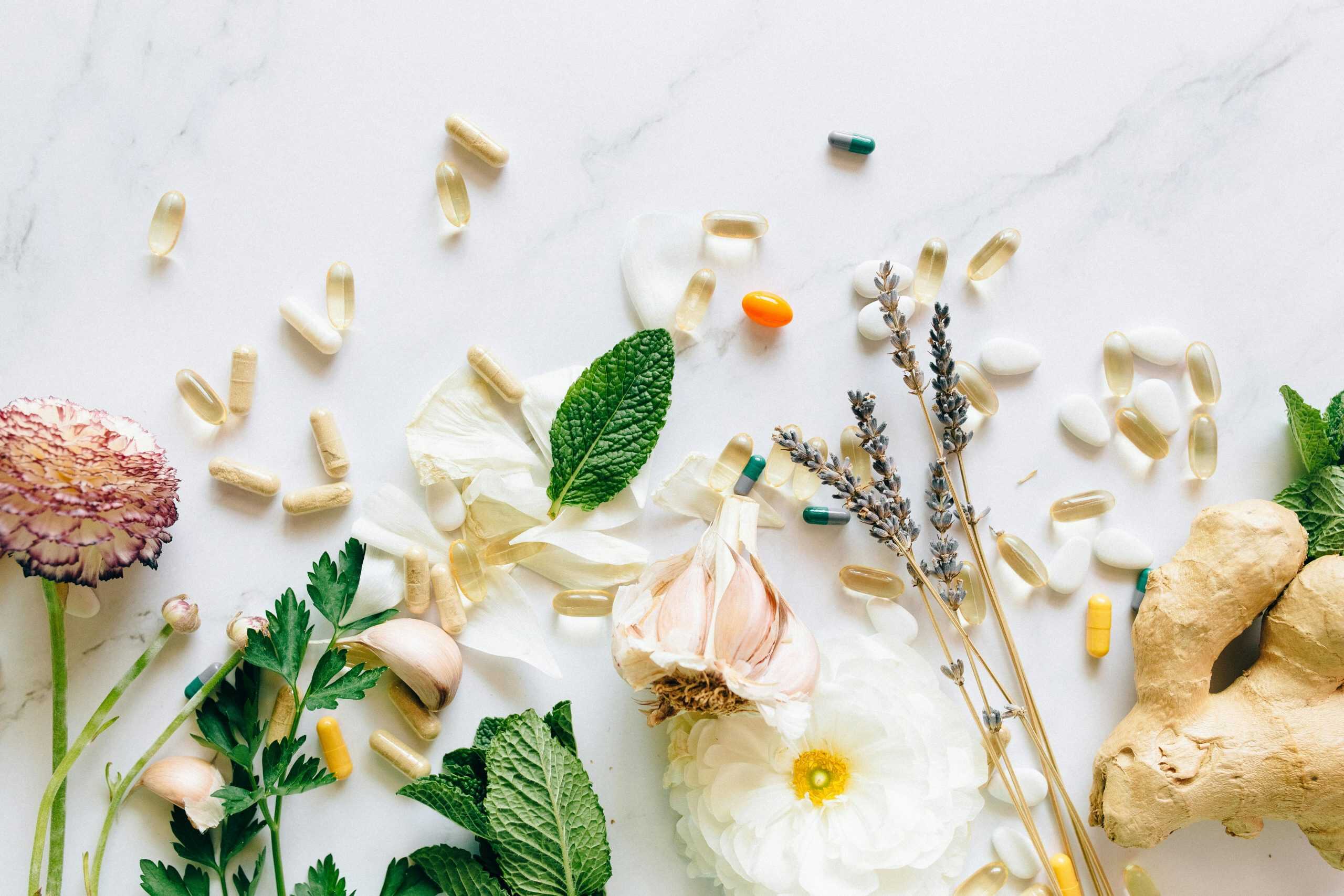 A flatlay of natural herbs, supplements, and flowers on a marble background. creatine