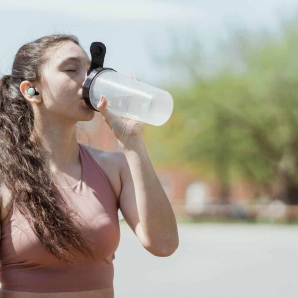 Young woman in sportswear drinks water outdoors, enjoying a sunny day, electrolyte, heat waves