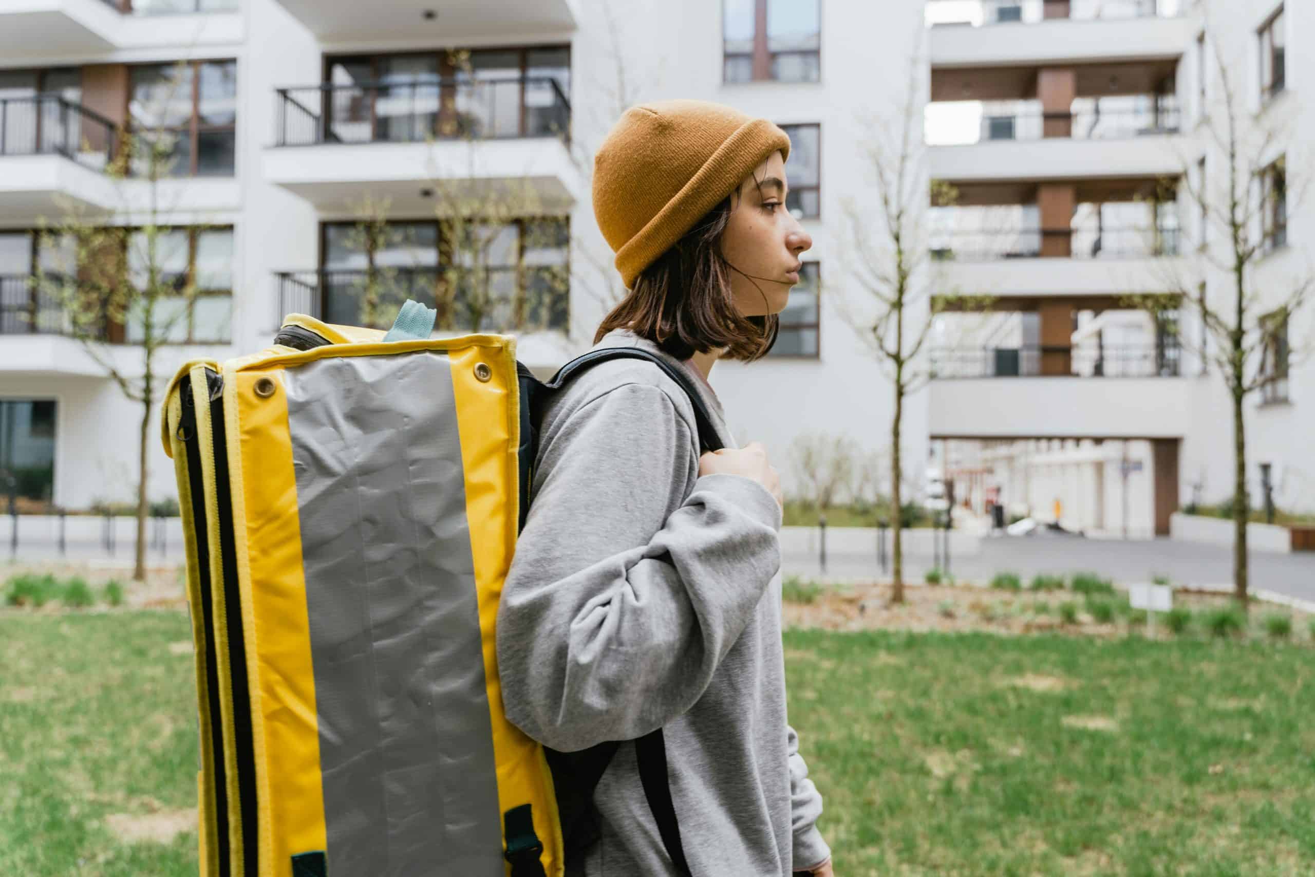 Woman in casual attire with a thermal delivery bag, walking in a modern city environment.