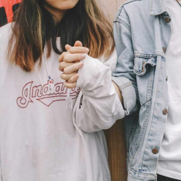 Young couple holding hands in casual attire, symbolizing love and togetherness.