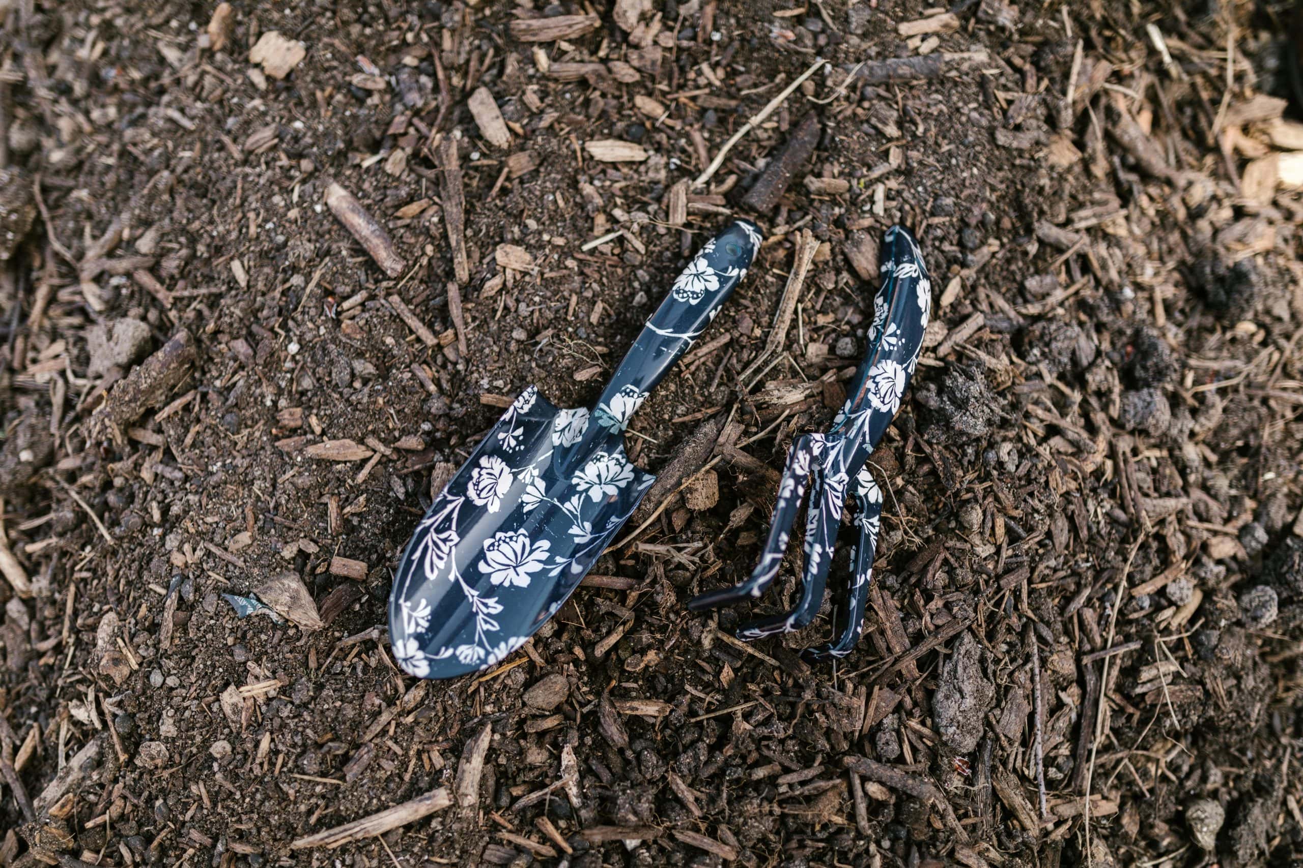 Close-up of floral patterned rake and shovel resting on soil, ideal for gardening themes. DIY Fertilizers, fall garden