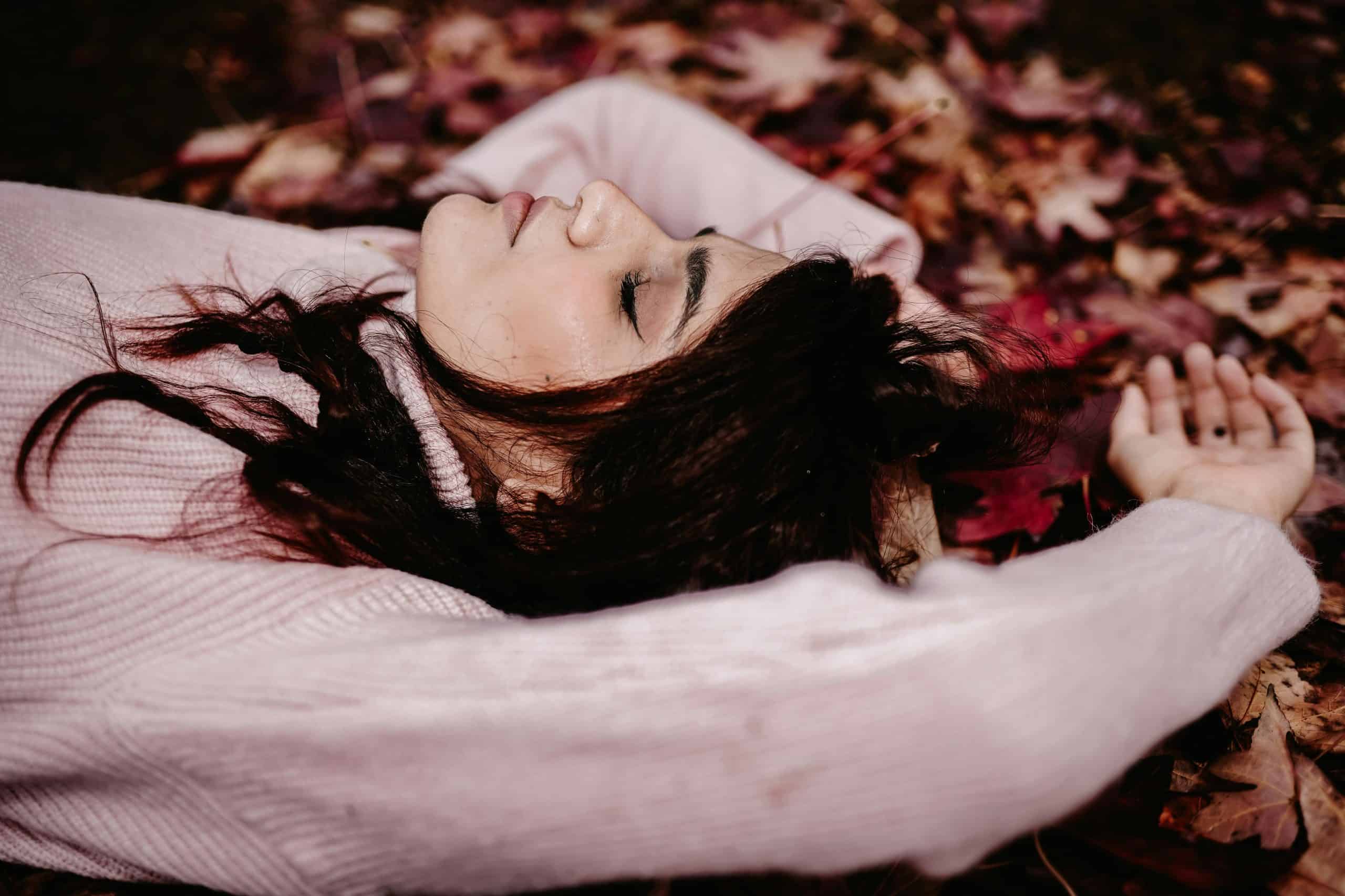 Woman in cozy sweater lying on colorful fallen leaves during autumn.