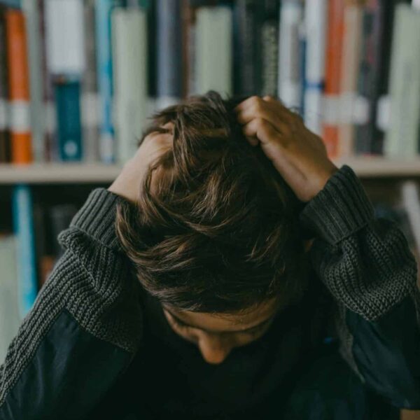 head Lice, children, kids hair, A child appears stressed and frustrated while seated in a library, holding their head.