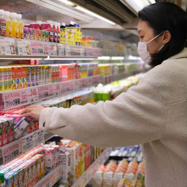 Masked woman shopping for beverages in a supermarket aisle, juice recall, unpasteurized