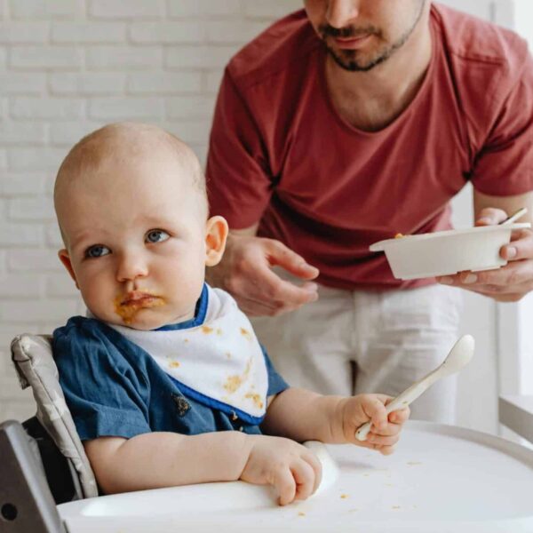 A father feeding his baby in a high chair, showcasing a nurturing family moment. baby food recall