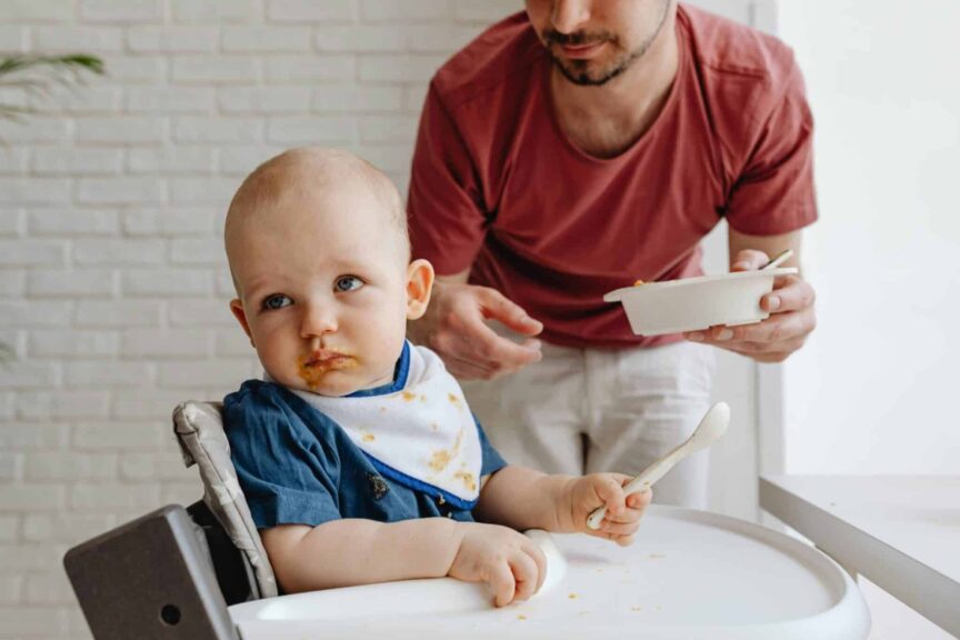 A father feeding his baby in a high chair, showcasing a nurturing family moment. baby food recall