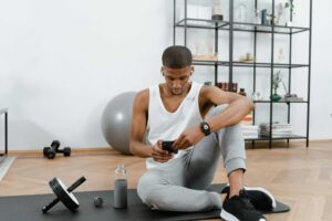 A man in sportswear using a smartphone on a yoga mat at home. Fitness and technology concept. at home gym fitness
