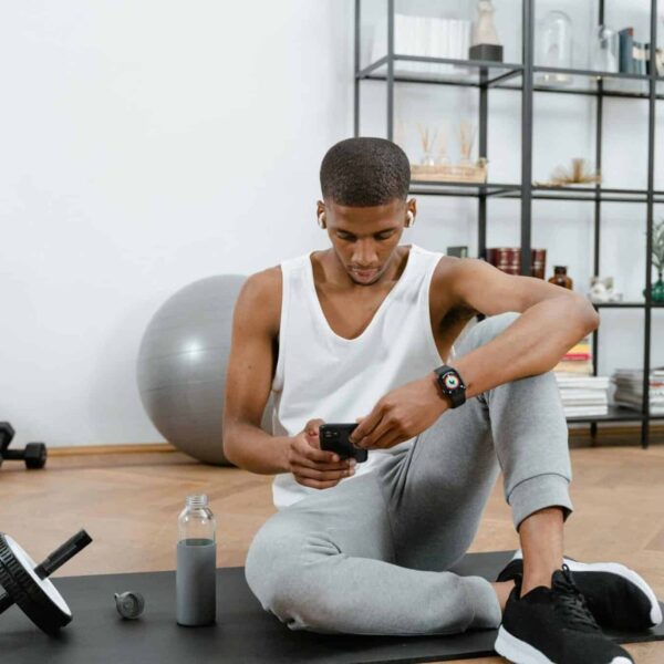 A man in sportswear using a smartphone on a yoga mat at home. Fitness and technology concept. at home gym fitness
