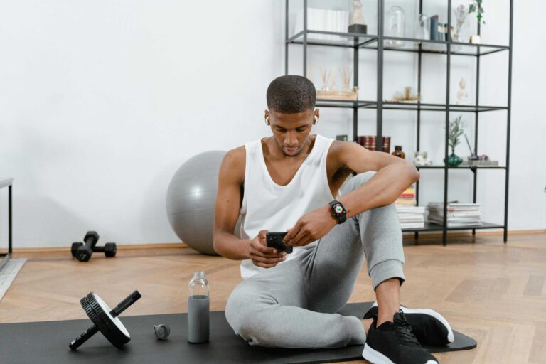 A man in sportswear using a smartphone on a yoga mat at home. Fitness and technology concept. at home gym fitness