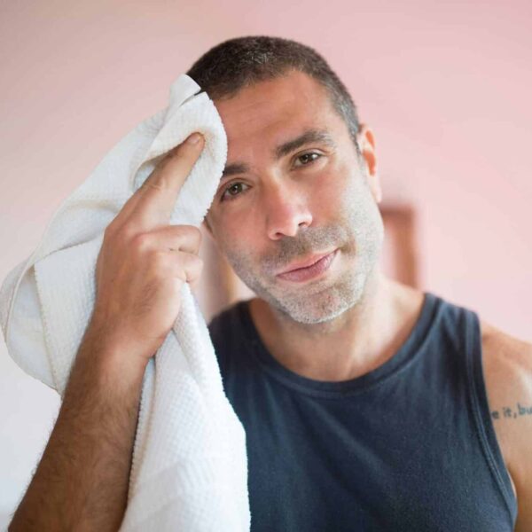 A man wipes sweat with a towel indoors, showcasing post-exercise relaxation. mental health medications excessive sweating