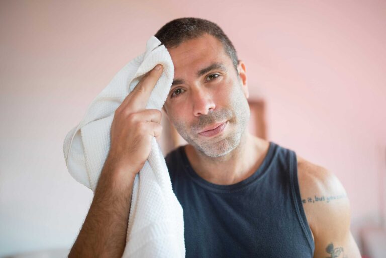A man wipes sweat with a towel indoors, showcasing post-exercise relaxation. mental health medications excessive sweating