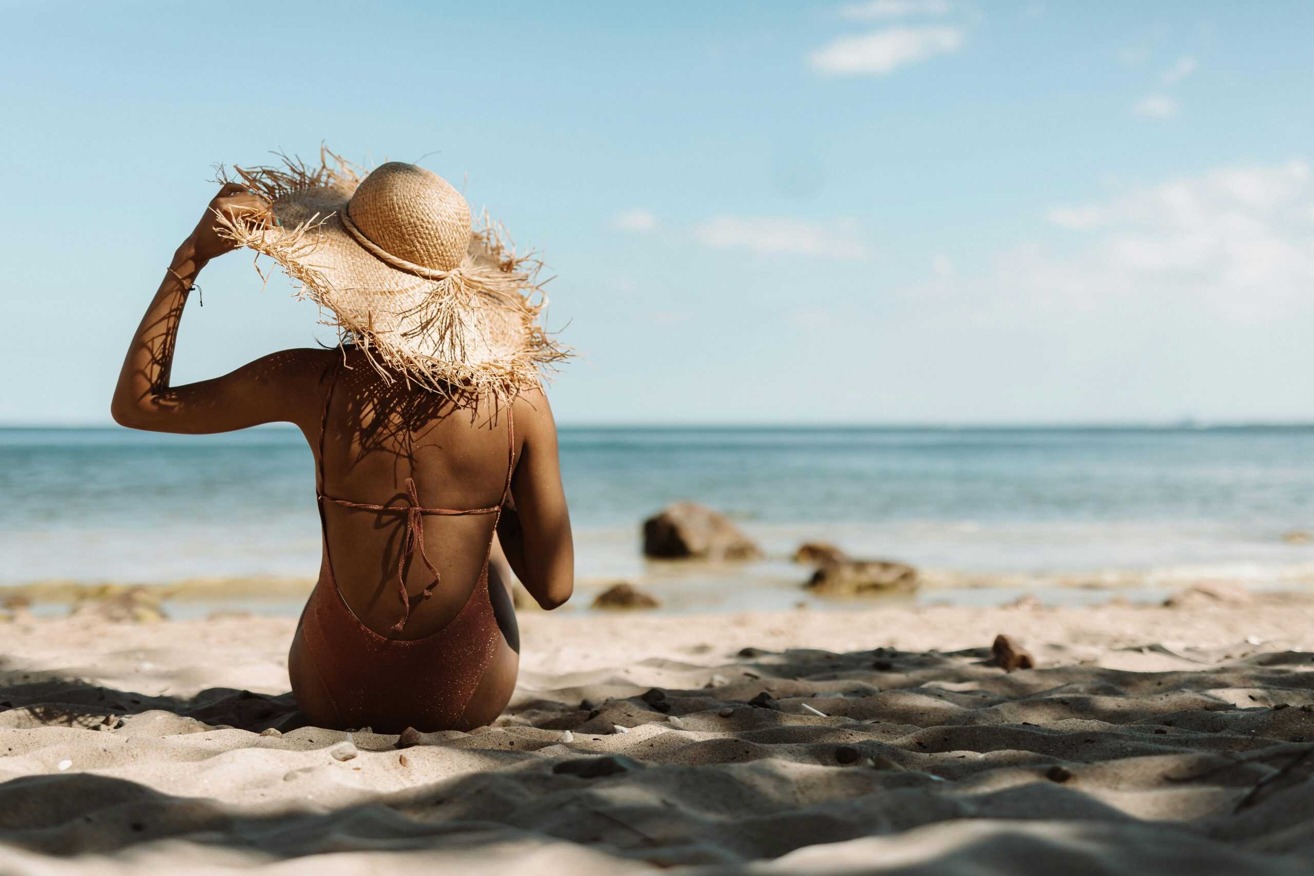 Back view of woman in straw hat enjoying a sunny day at the beach.