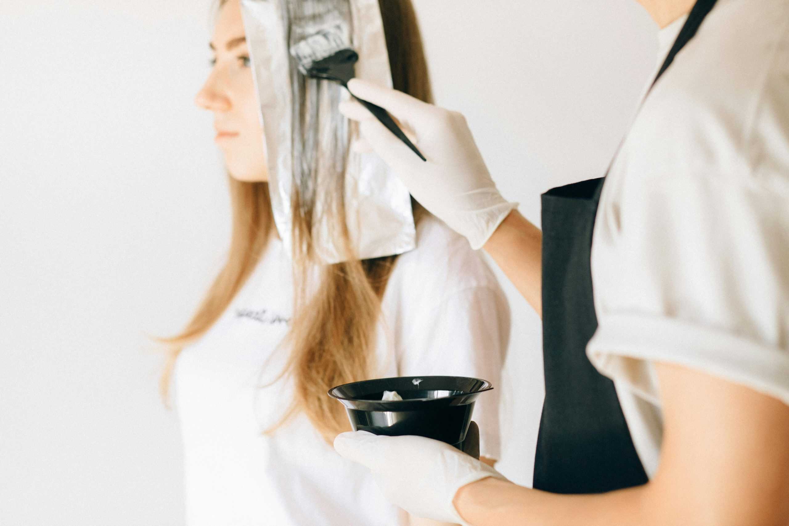 Hairdresser applying color to woman's hair in salon using brush and foil technique.