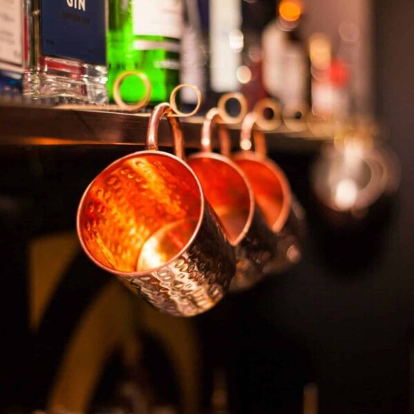 Close-up of copper mugs with blurred bar bottles. Warm glow and bokeh effect. Fall cocktails