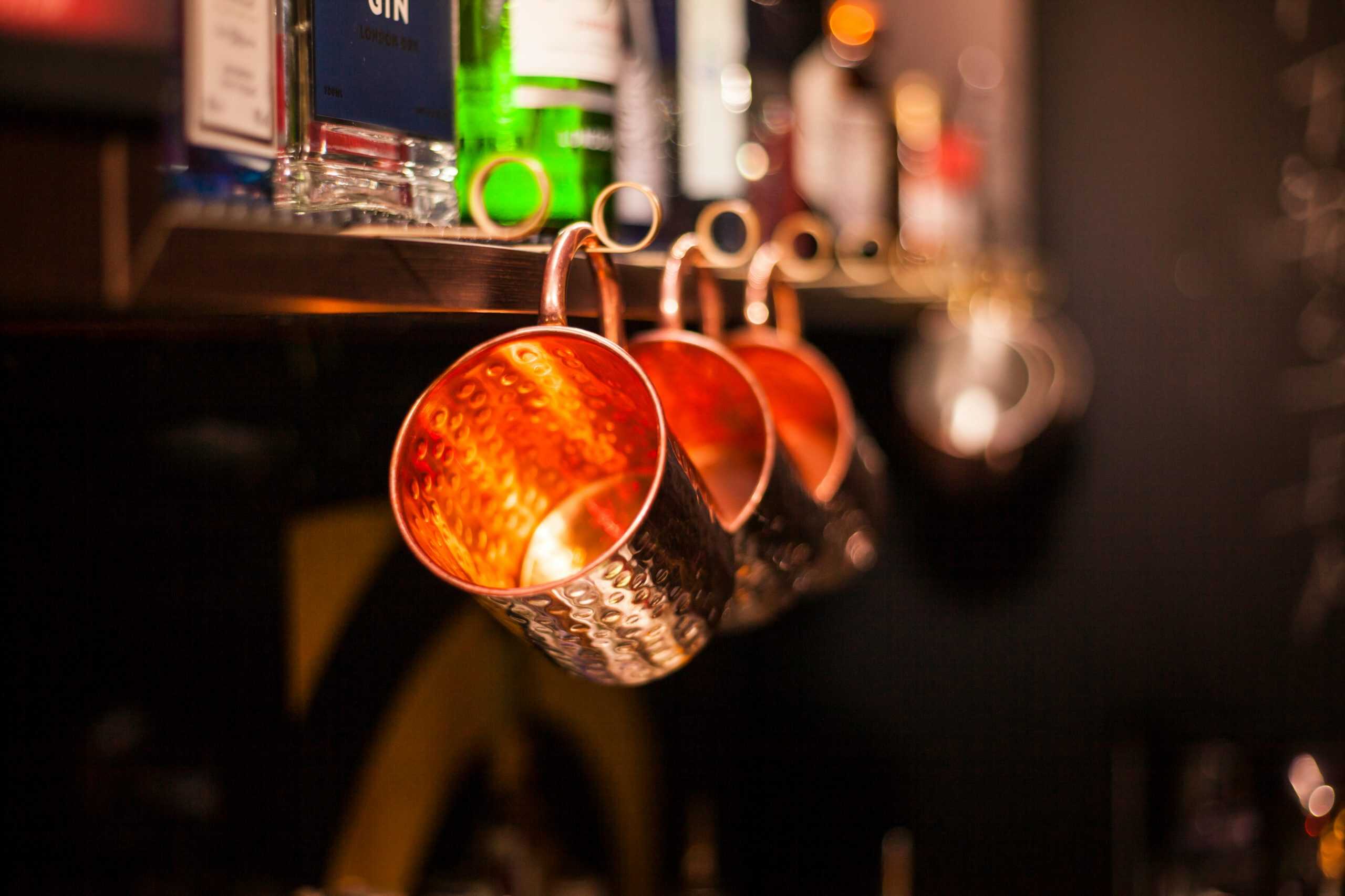Close-up of copper mugs with blurred bar bottles. Warm glow and bokeh effect. Fall cocktails