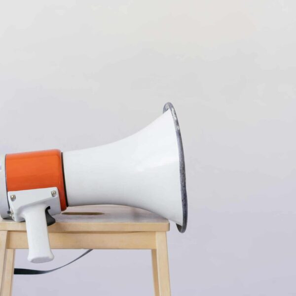 outspoken, Close-up of a megaphone resting on a wooden chair with a minimalist background.
