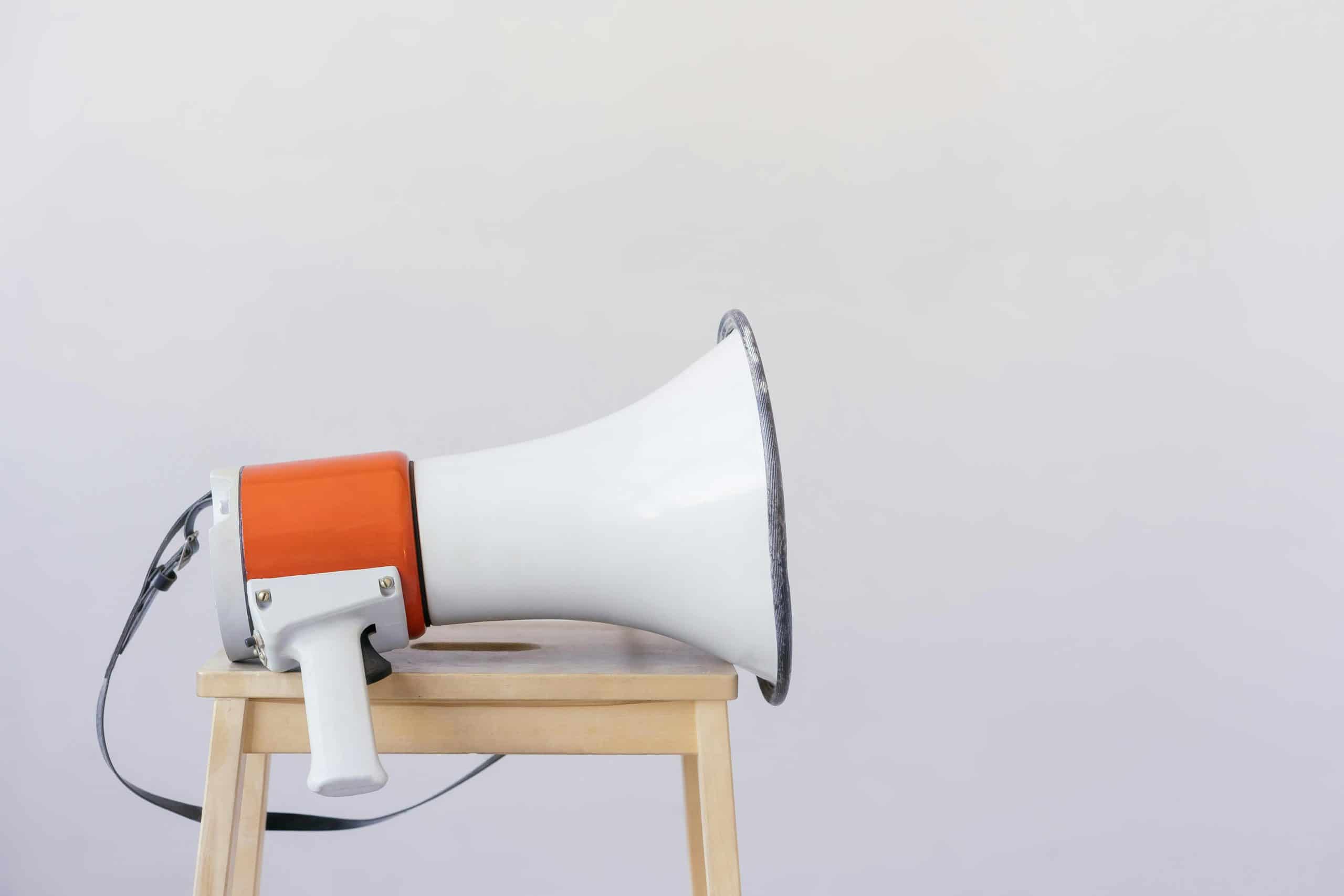 outspoken, Close-up of a megaphone resting on a wooden chair with a minimalist background.