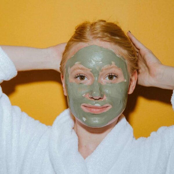 Woman enjoying self-care with a green face mask against a yellow background.