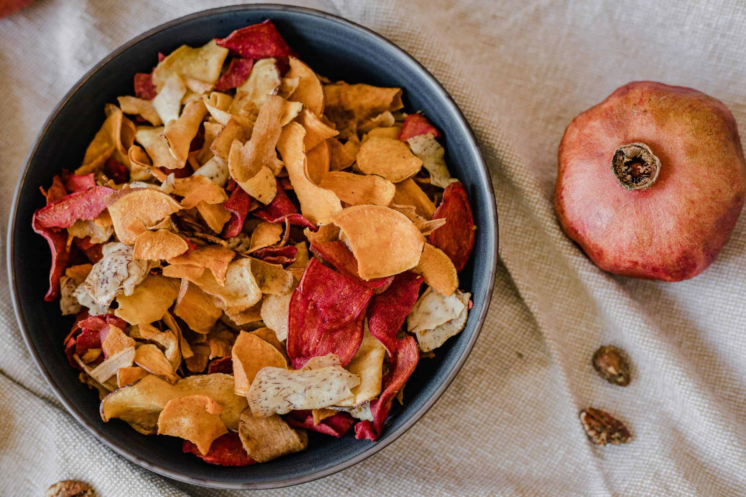 healthy chips, recipes, A stylish presentation of healthy dried fruit chips in a bowl with a pomegranate on textile background.