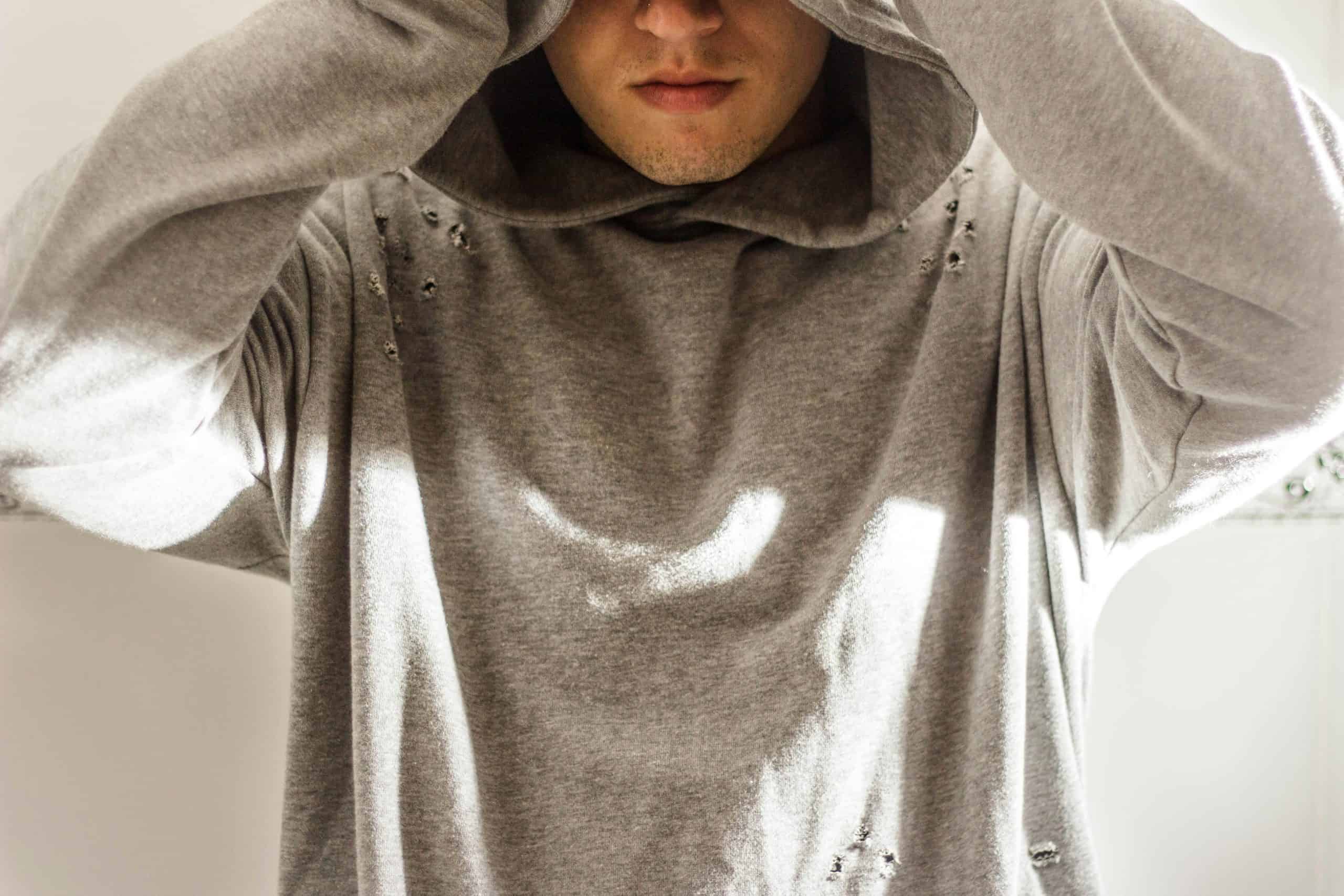 Close-up of a man in a gray hoodie, face partially obscured, soft light indoors.
