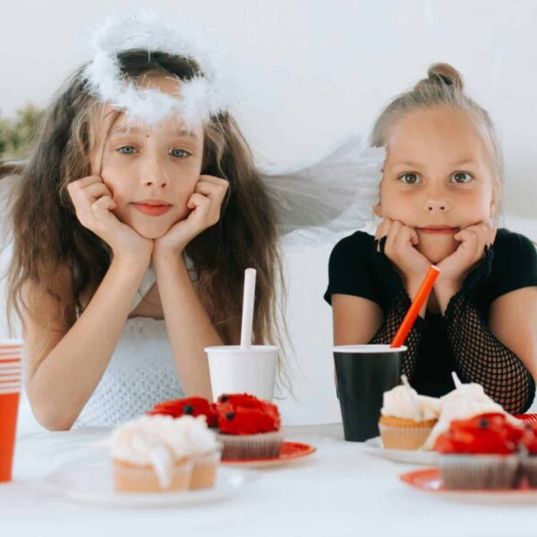 Two young girls dressed as an angel and demon at a Halloween party with cupcakes. fall drinks for kids, kids drinks,