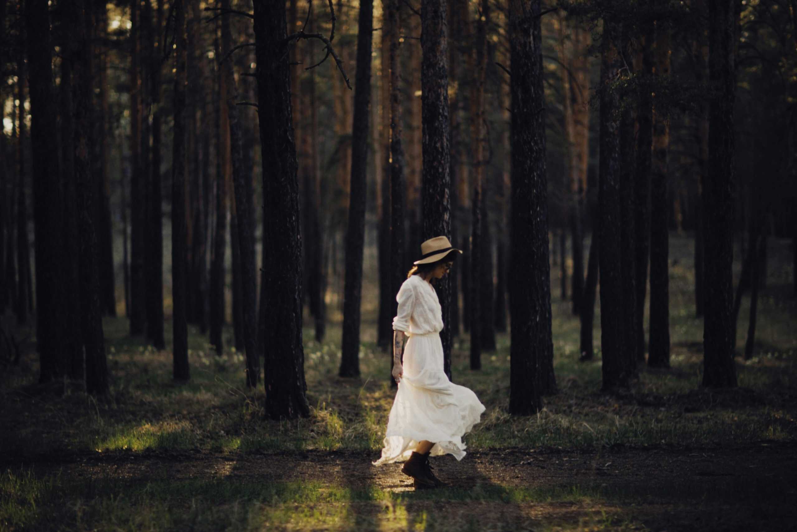 Woman in a white dress walking through a tranquil forest at sunset, embodying freedom and individuality. Daily devotion