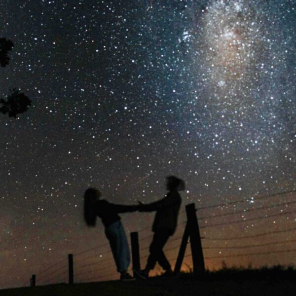 Silhouetted couple holding hands under a starry Milky Way sky, creating a romantic scene.
