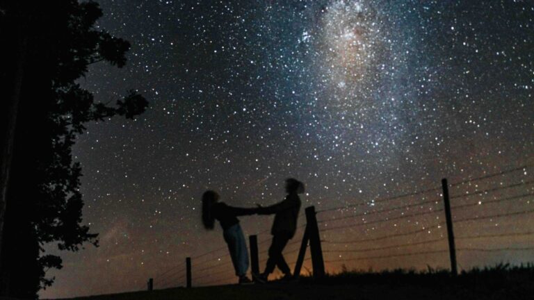 Silhouetted couple holding hands under a starry Milky Way sky, creating a romantic scene.