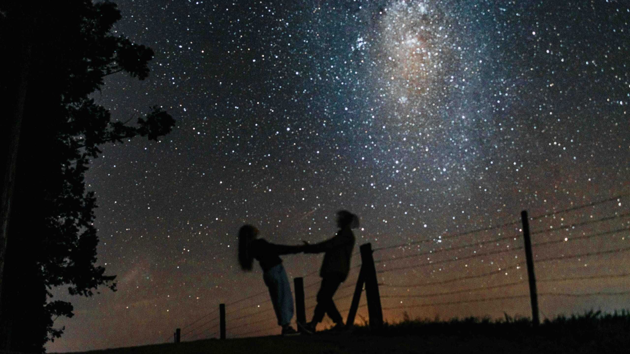 Silhouetted couple holding hands under a starry Milky Way sky, creating a romantic scene.