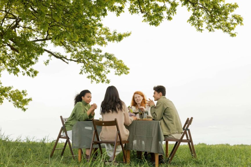 Gen Z, intentional, A diverse group of friends at an outdoor picnic, enjoying food and conversation under a tree.