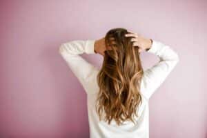 Back view of a woman with elegant long brown hair against a pink wall, showcasing stylish hair design. hair masks
